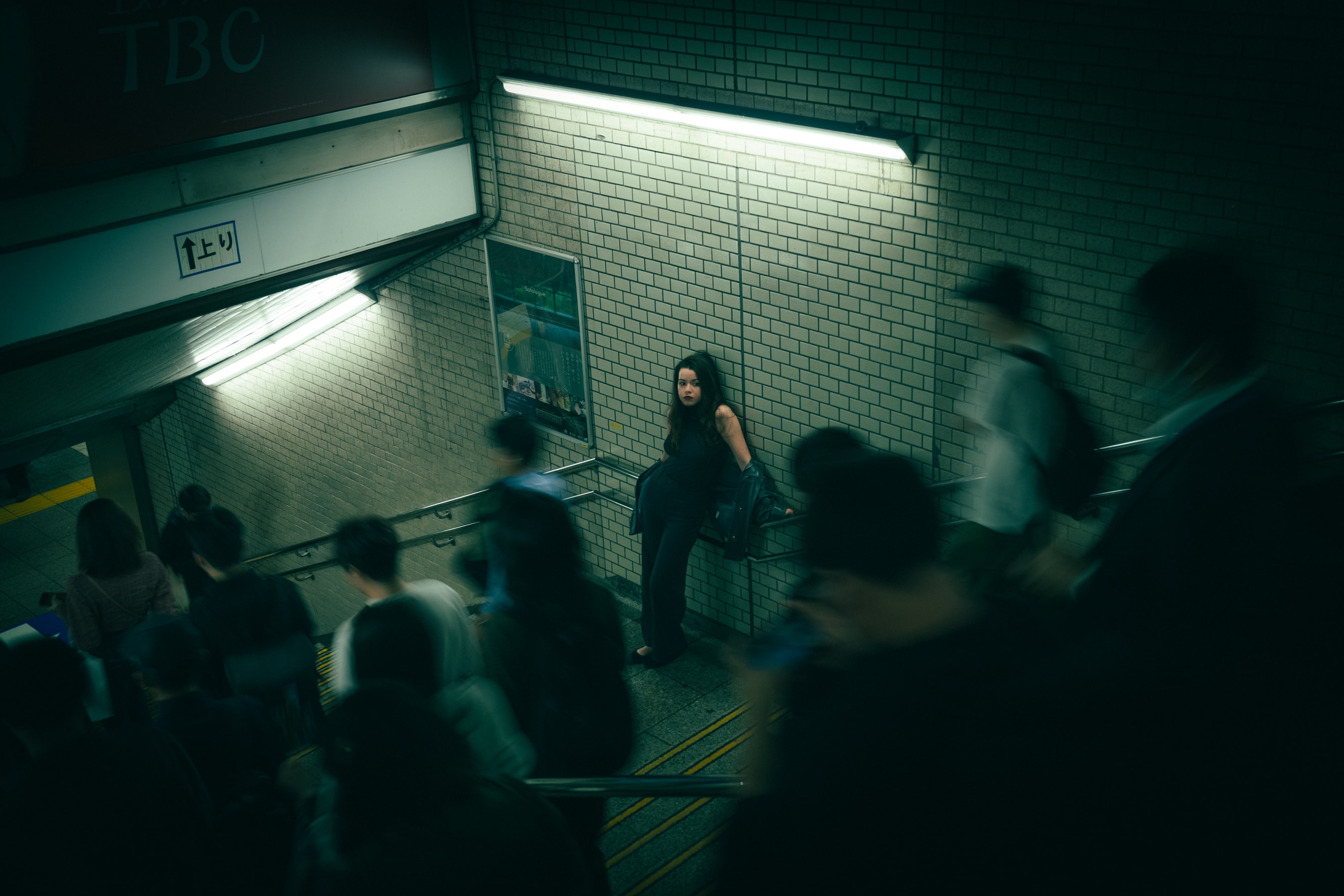 A pause on the stairs, rush hour moving around her.