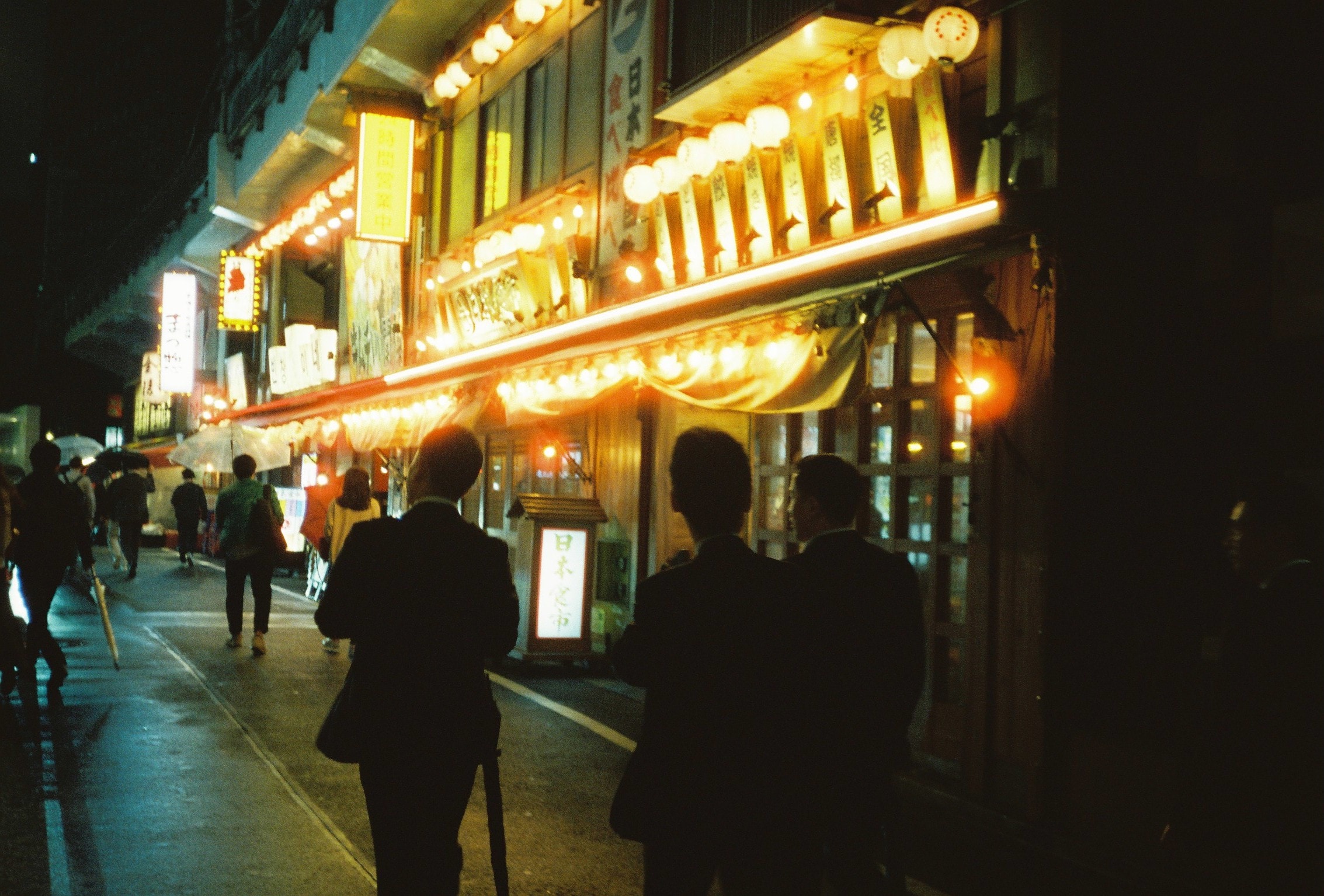 Three suits under paper lanterns, waiting for a table.