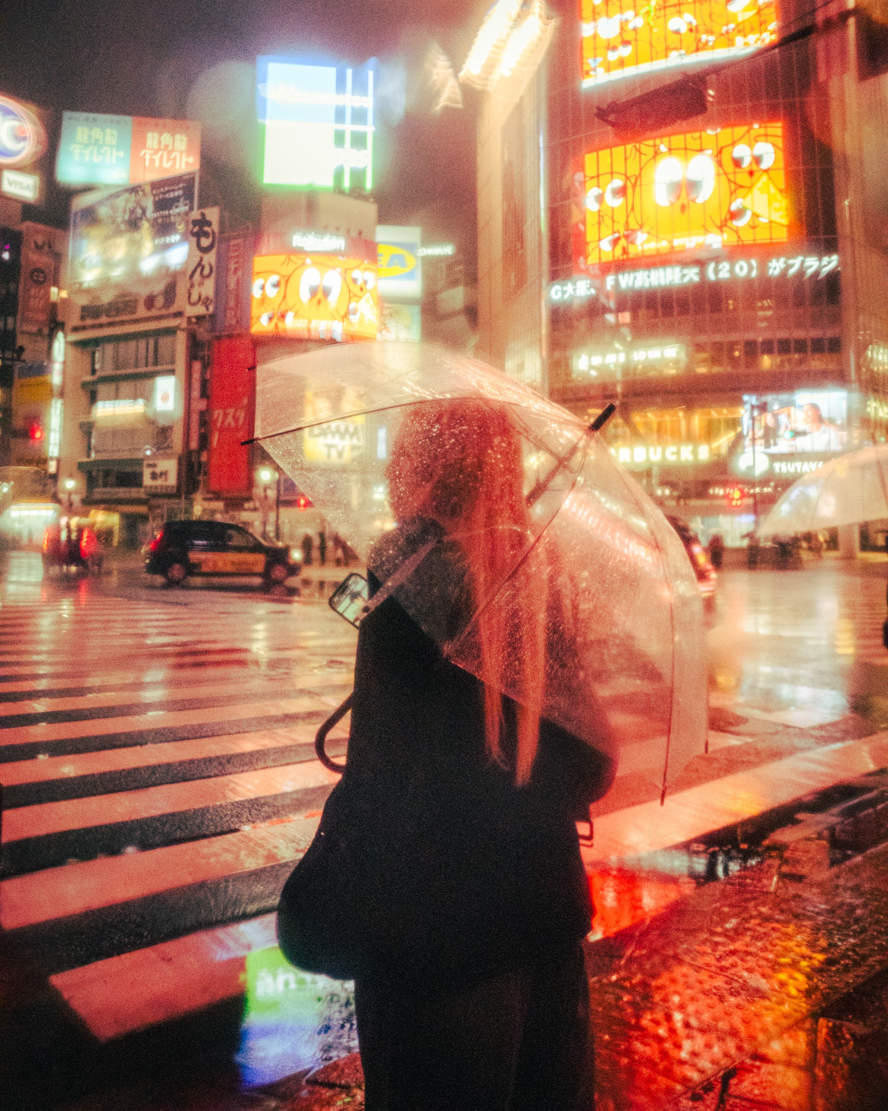 Rain on the crossing, an umbrella catching the neon.