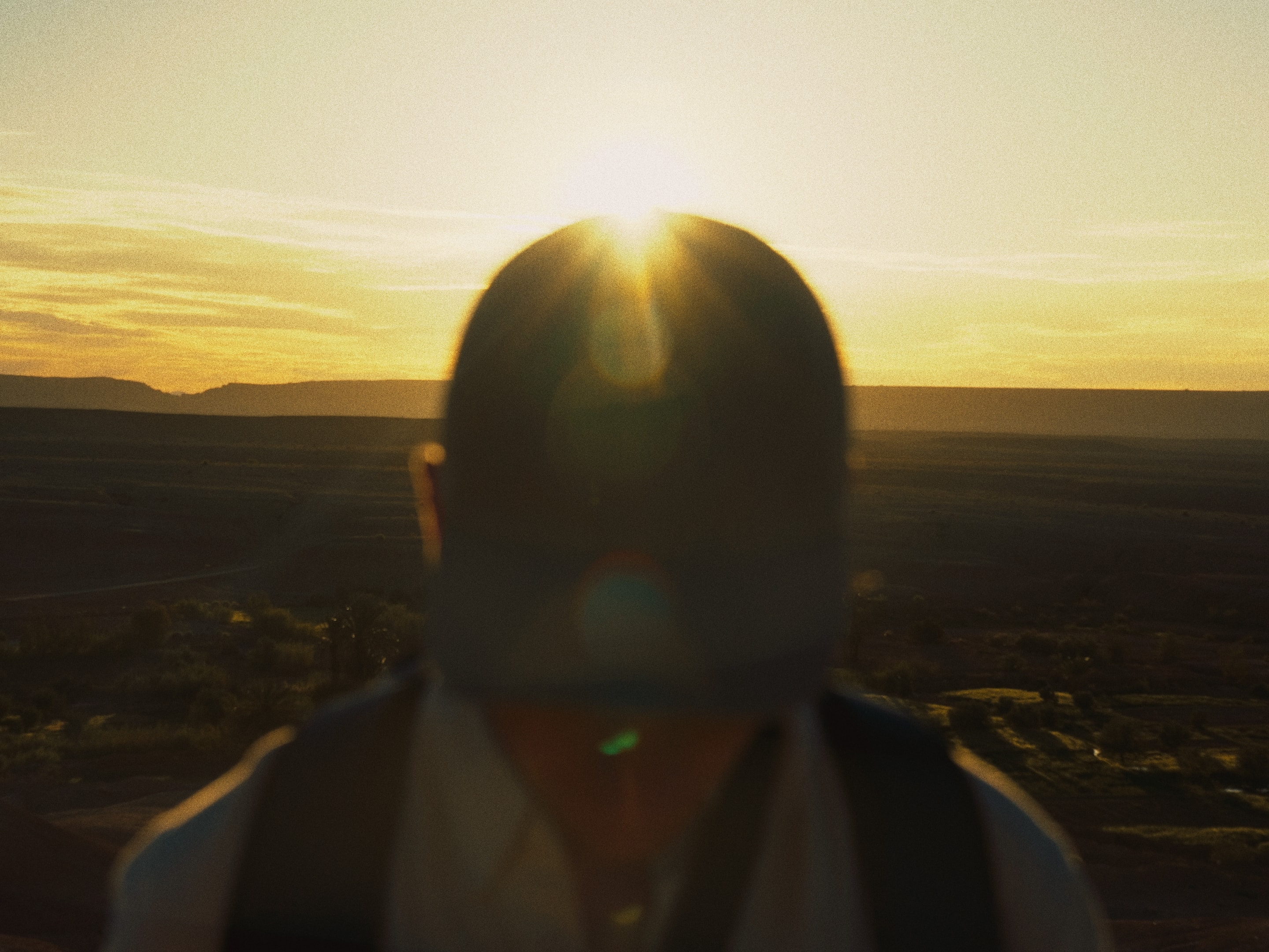 The sun breaks behind him, desert stretching to the horizon.